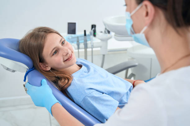 Pleased teenage patient lying in dental chair and looking at pediatric dentist Soft Tissue Injury Treatment McClane Dentistry